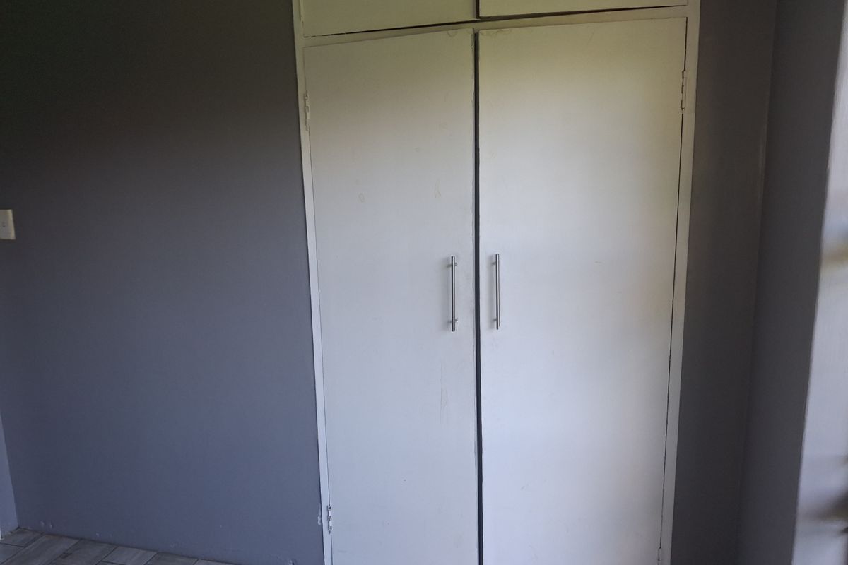 A bedroom interior featuring built-in cupboards with white doors and modern handles, set against a grey wall and tiled flooring.