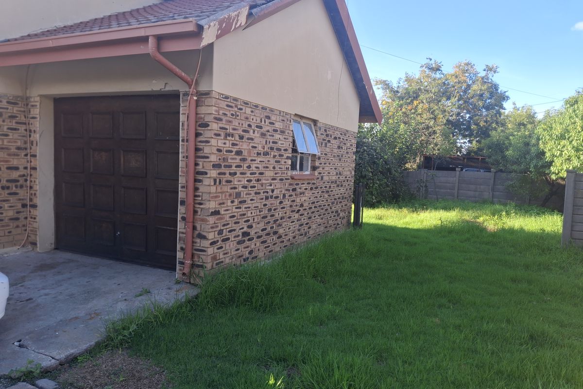 Exterior view of the property showing a single garage with brick facade, tiled roof, and an adjacent grassed garden area.