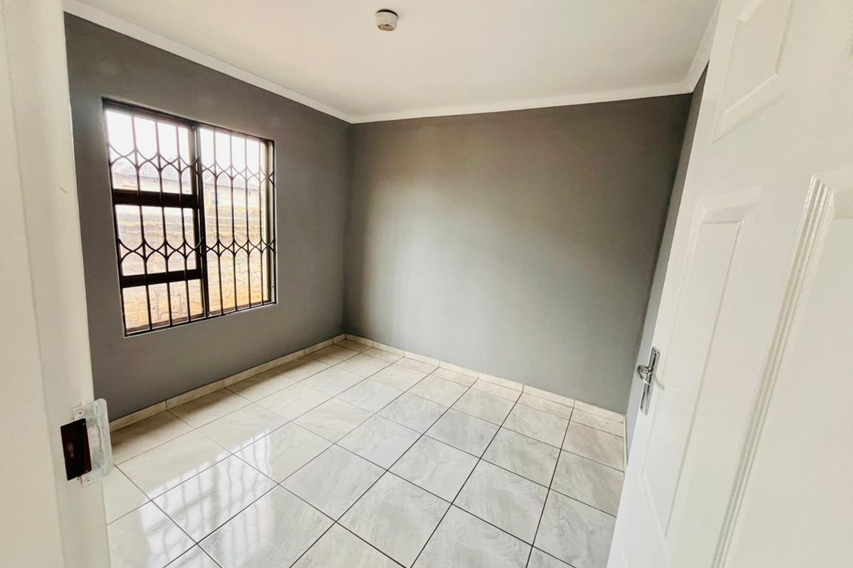 A clean, empty bedroom featuring neutral grey walls, light-colored tiled flooring, and a window fitted with security bars.