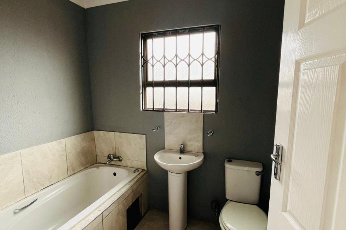 A functional bathroom featuring a bathtub with tiled surround, pedestal basin, and toilet, finished with neutral wall tones and tiled flooring.