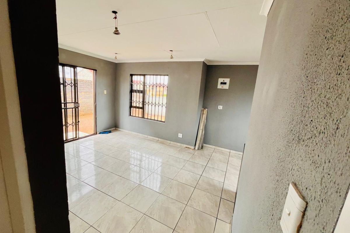 A bright, open-plan living area featuring neutral grey walls, large ceramic floor tiles, and security gates on the windows and sliding door.