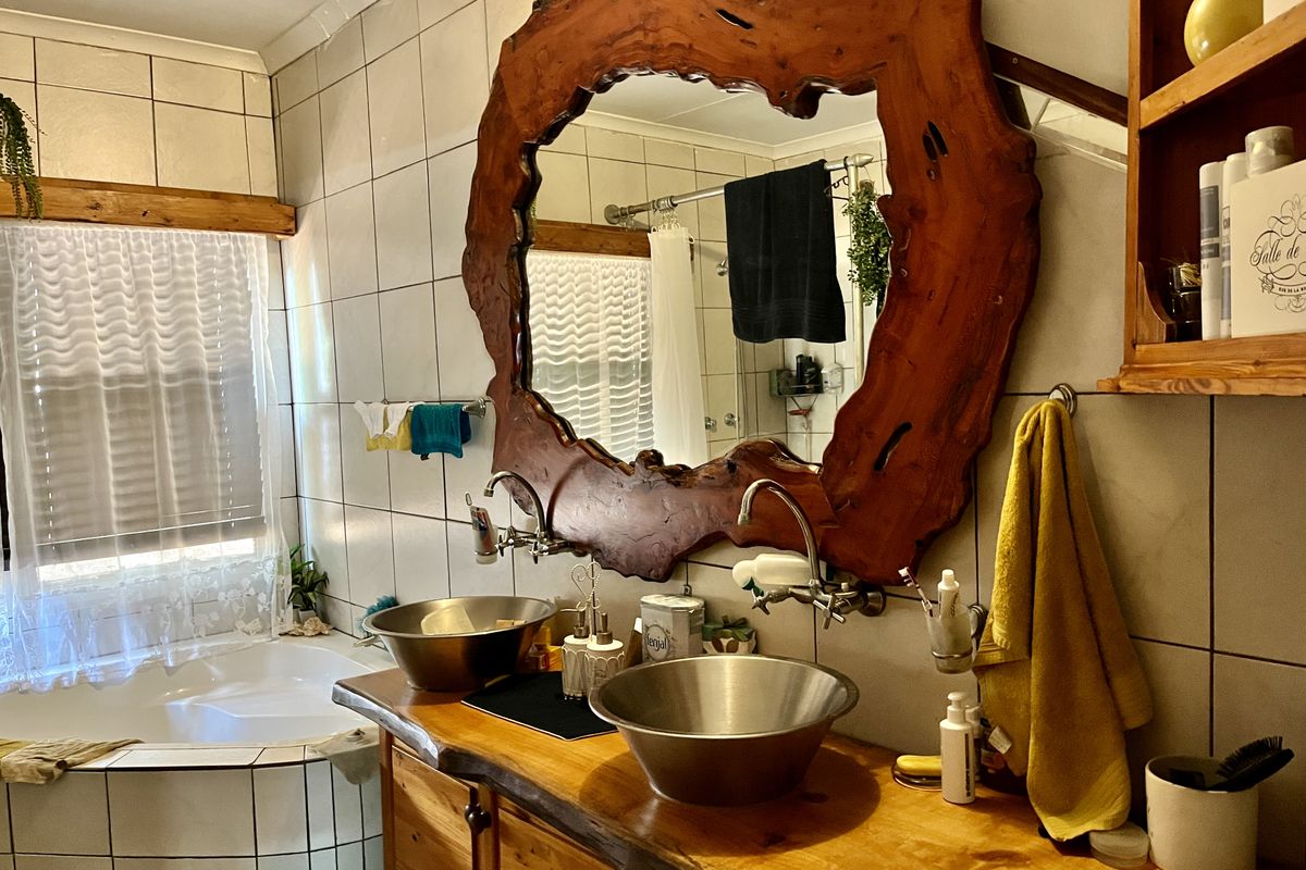 Bathroom featuring a double vanity with stainless steel vessel sinks, a large live-edge wood mirror frame, and a corner bathtub with tiled surround.