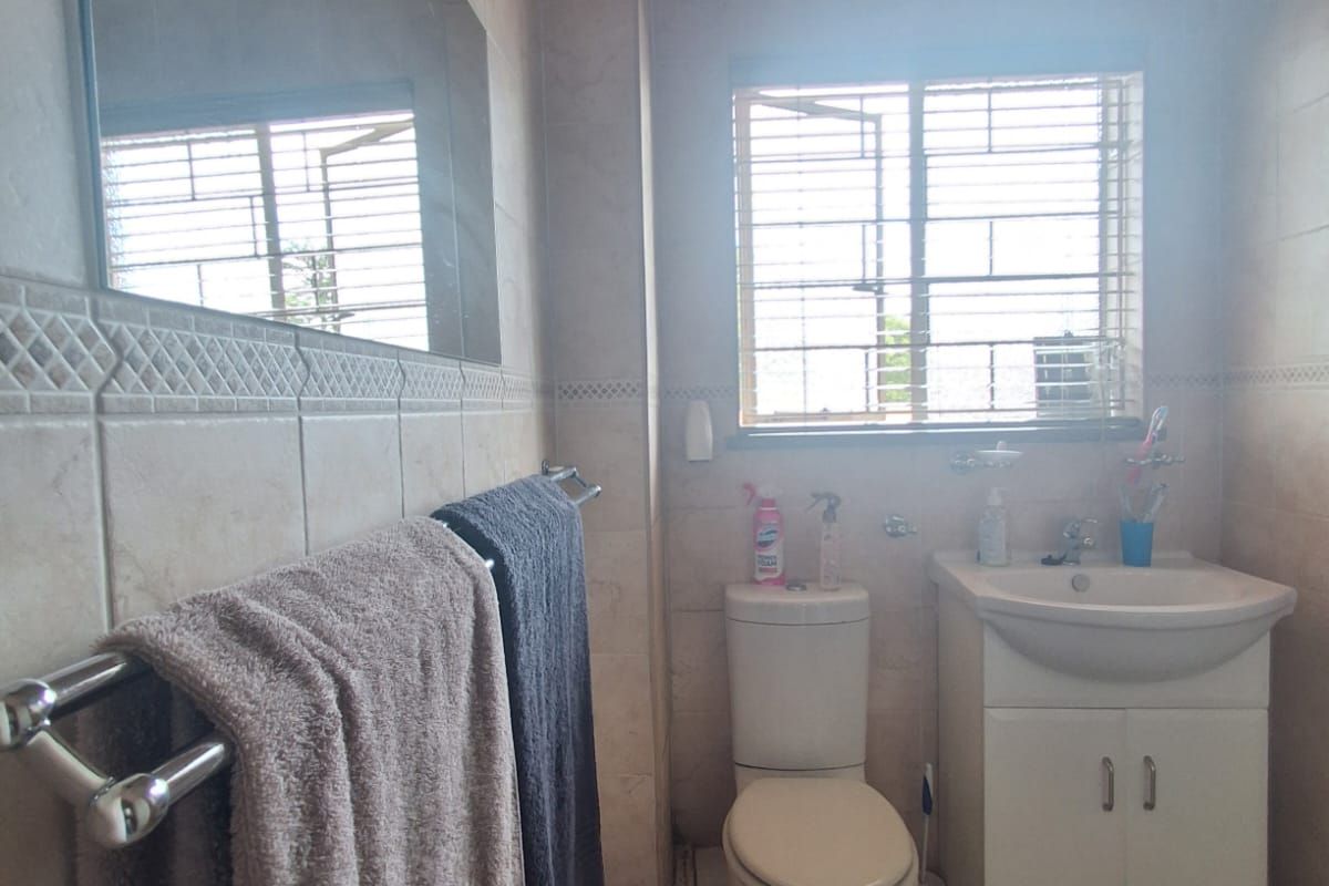 A functional bathroom featuring tiled walls and flooring, a pedestal vanity with basin, a toilet, and a window with security bars.