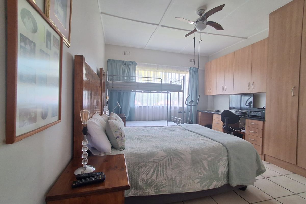 A functional bedroom featuring extensive built-in wooden cabinetry, a ceiling fan, and tiled flooring, providing ample storage and living space.
