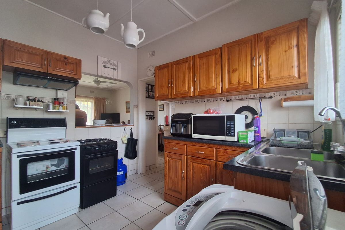 Functional kitchen featuring wooden cabinetry, tiled flooring, double basin sink, and space for a freestanding stove and washing machine.