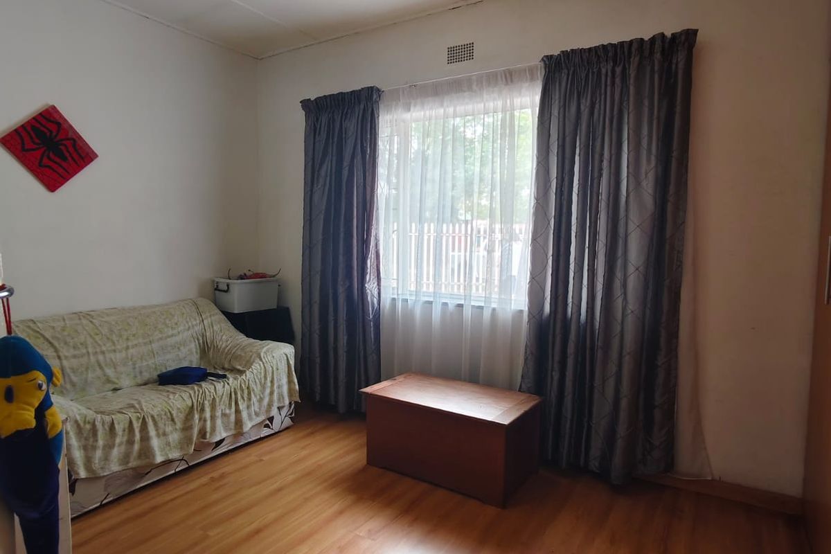 A bedroom featuring laminate wood flooring, a central ceiling light fixture, and a window with curtain tracks.