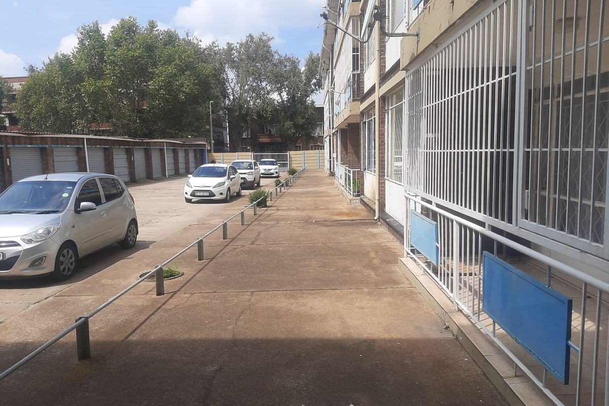 Exterior view of the flat complex featuring a paved walkway, metal security railings, and a row of garage units.