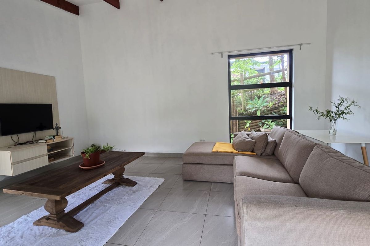 A bright living room featuring large windows, tiled flooring, and exposed ceiling beams, offering a comfortable and functional space.