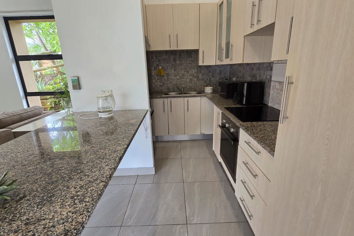A functional kitchen featuring light wood cabinetry, granite countertops, a built-in oven, hob, and a breakfast bar overlooking the living area.