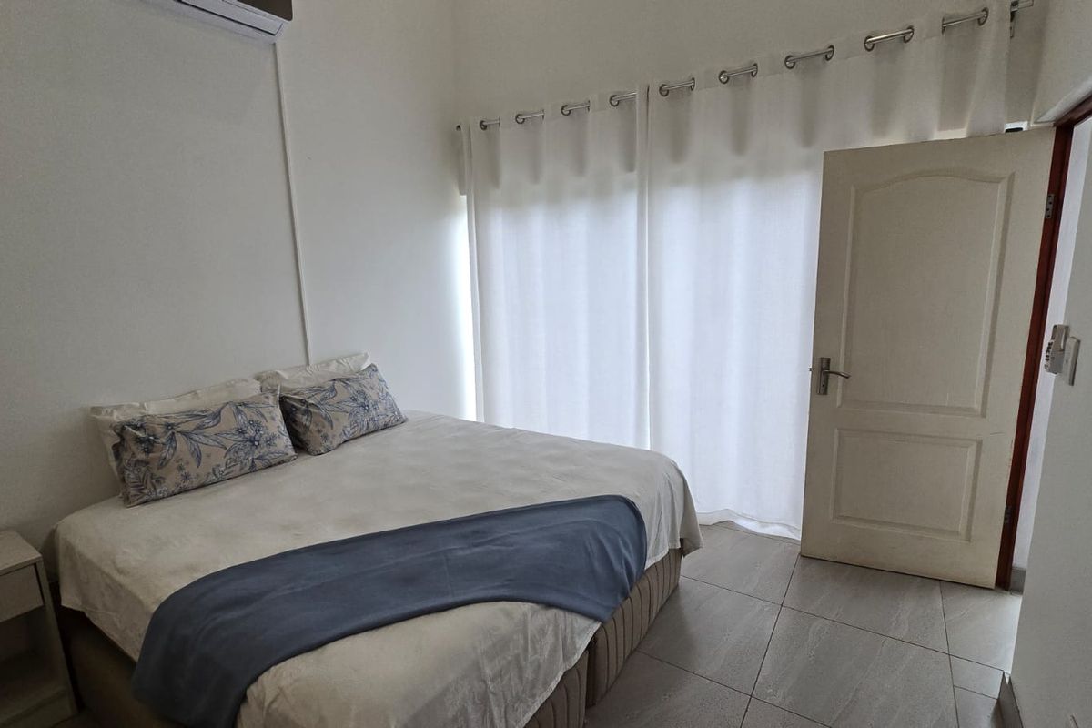 A bright bedroom featuring tiled flooring, a wall-mounted air conditioning unit, and direct access through a door.