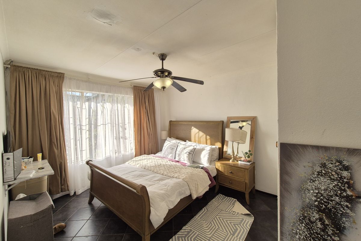 A well-lit bedroom featuring dark tiled flooring, a central ceiling fan, and large windows with curtains.