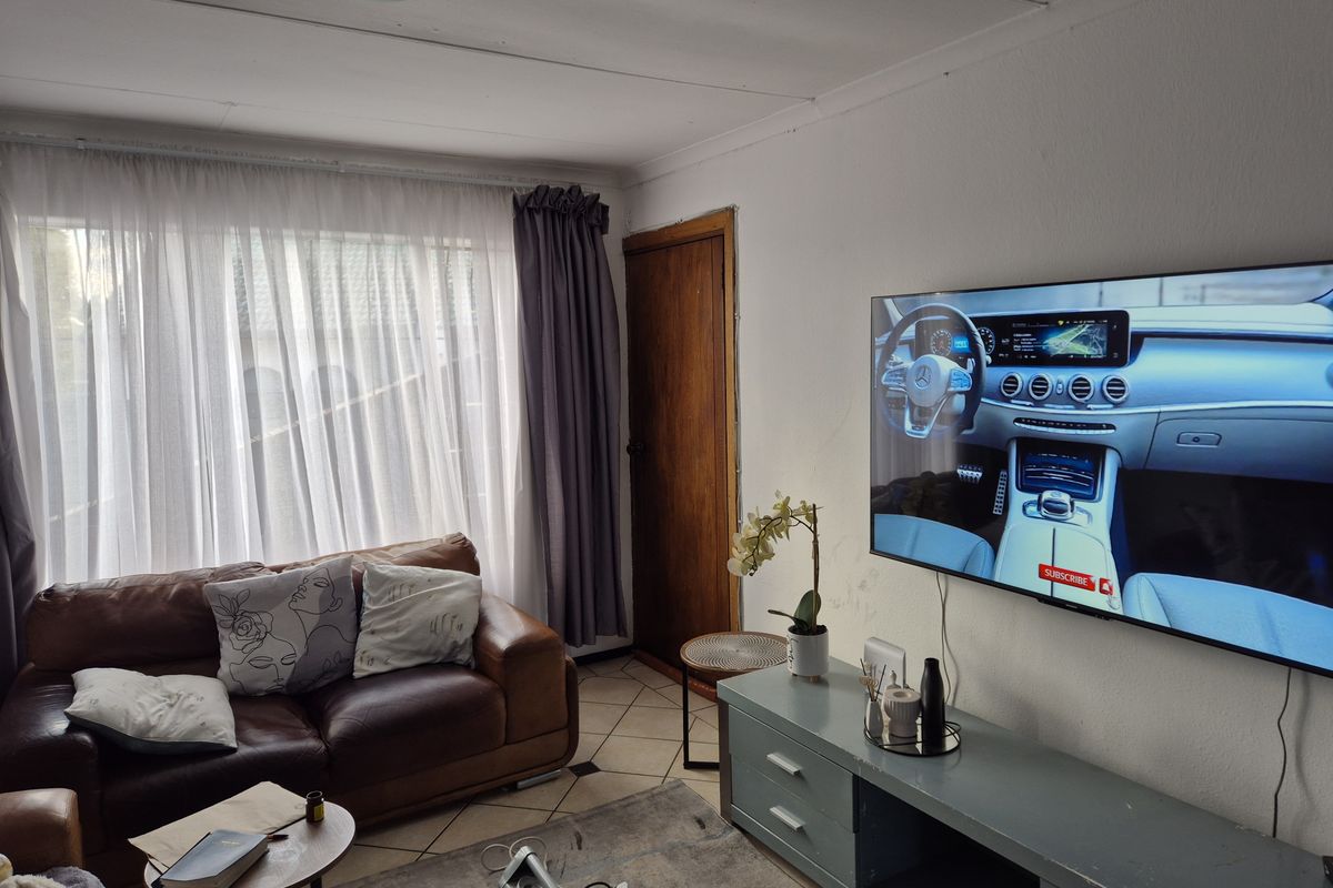 A living room featuring tiled flooring, a large window with curtains, and a wall-mounted television setup.