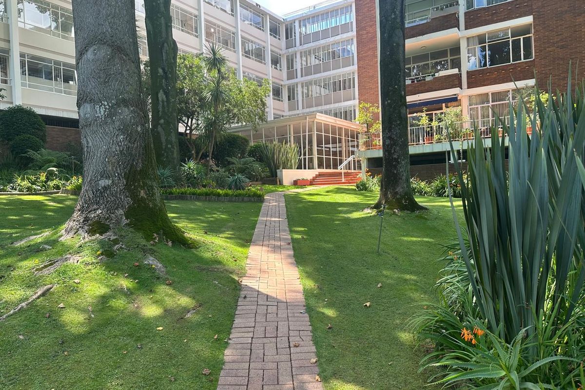 A view of the communal garden area featuring a brick pathway leading towards the residential apartment building facade.