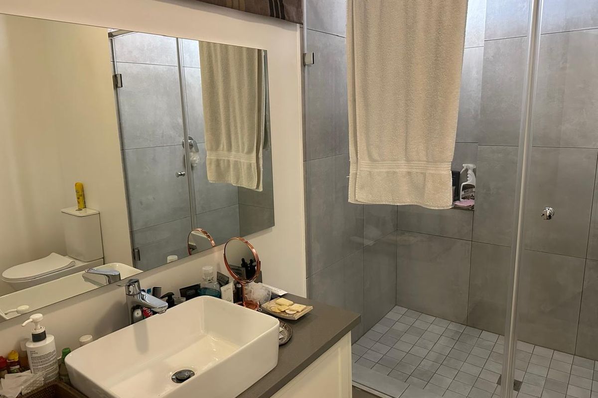 Modern bathroom featuring a walk-in shower with glass enclosure, large format grey wall tiles, and a contemporary countertop basin vanity.