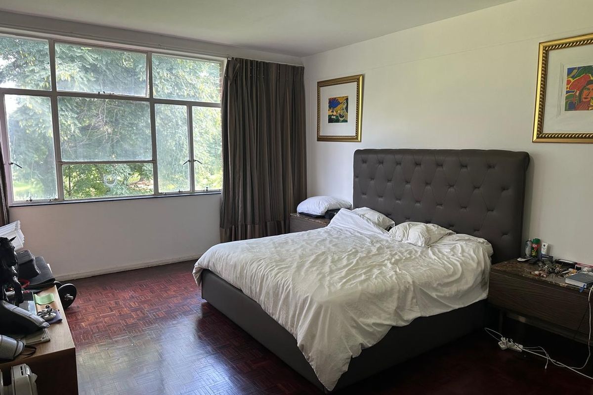 Spacious bedroom featuring original parquet flooring, large windows providing natural light, and neutral wall finishes.