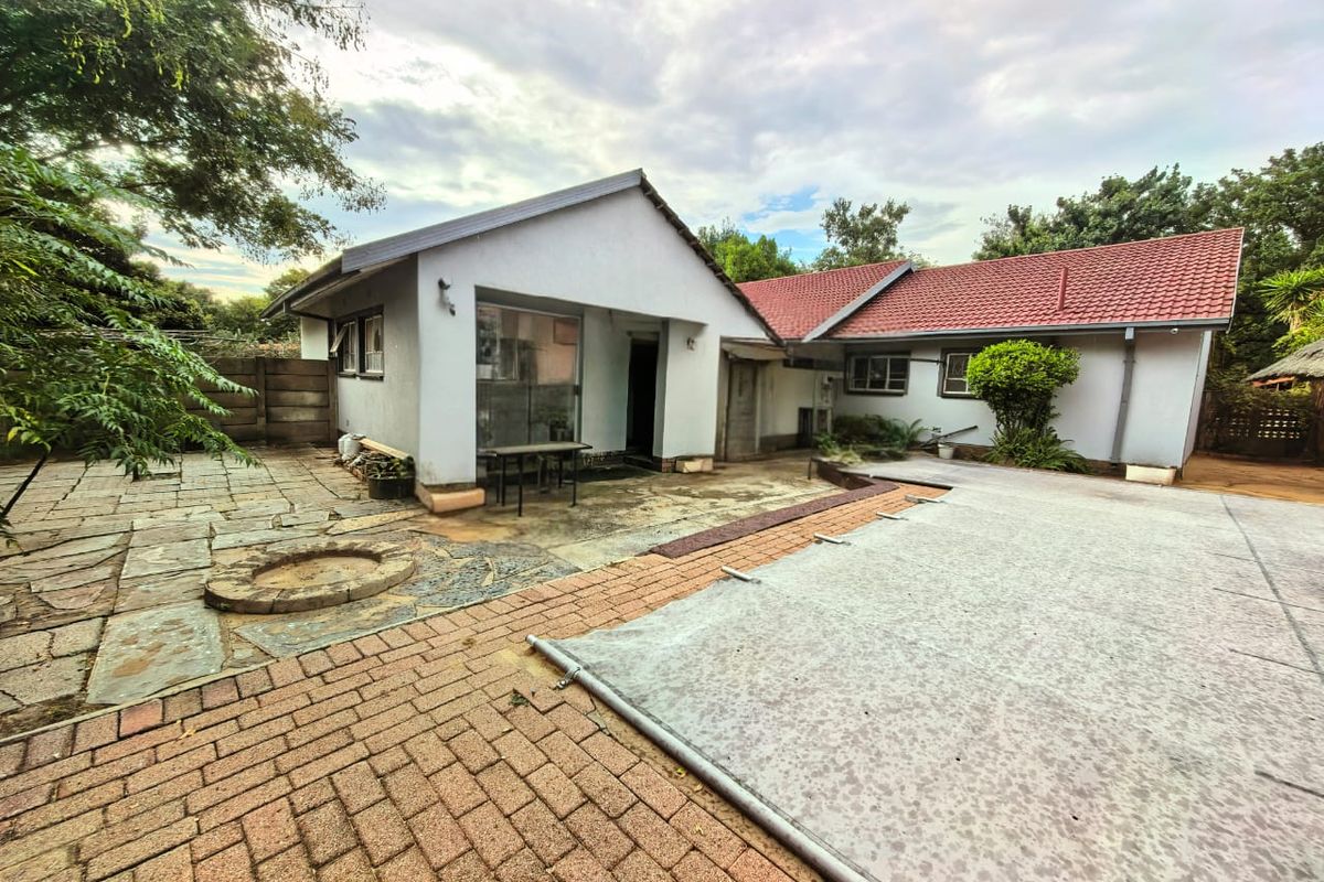Rear exterior view of the house featuring a paved patio area, a covered swimming pool, and established garden surroundings.