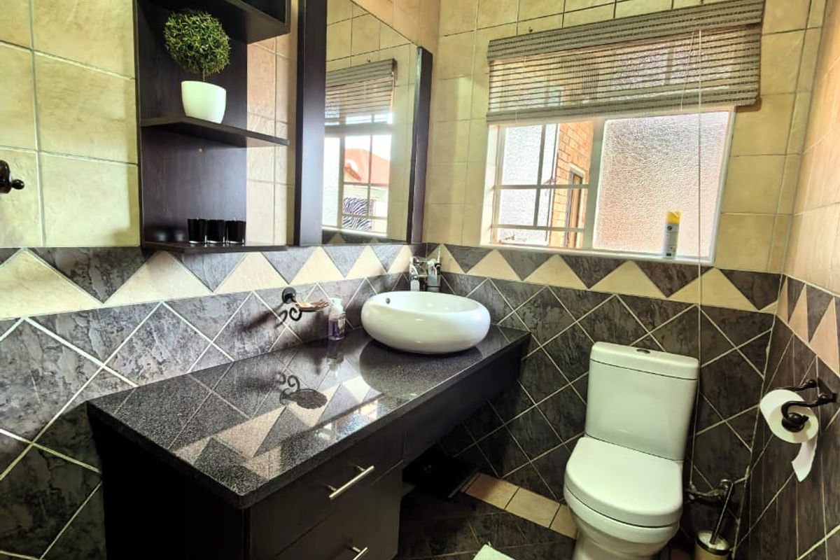 A compact bathroom featuring a dark granite vanity top, vessel sink, wall-mounted shelving, and tiled walls with a decorative border.