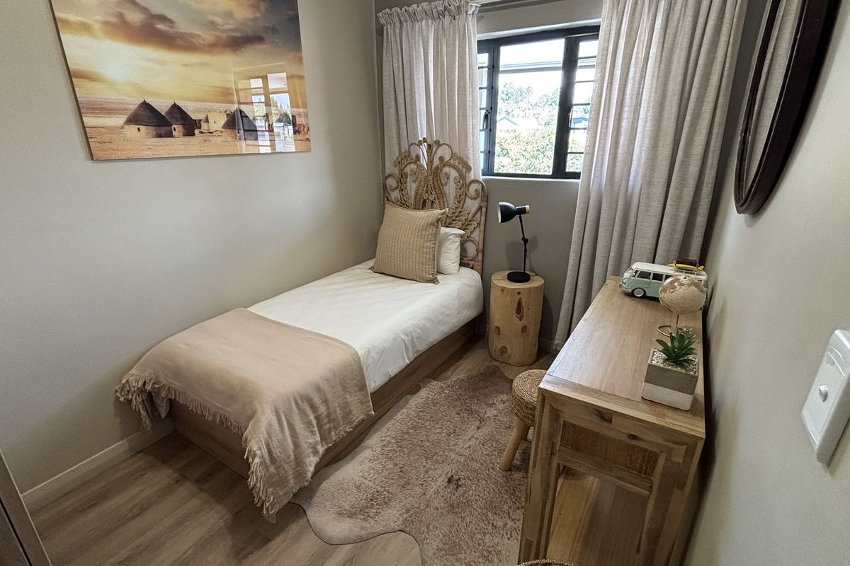 A compact bedroom featuring light wood-look flooring, neutral wall tones, and a window with security bars.