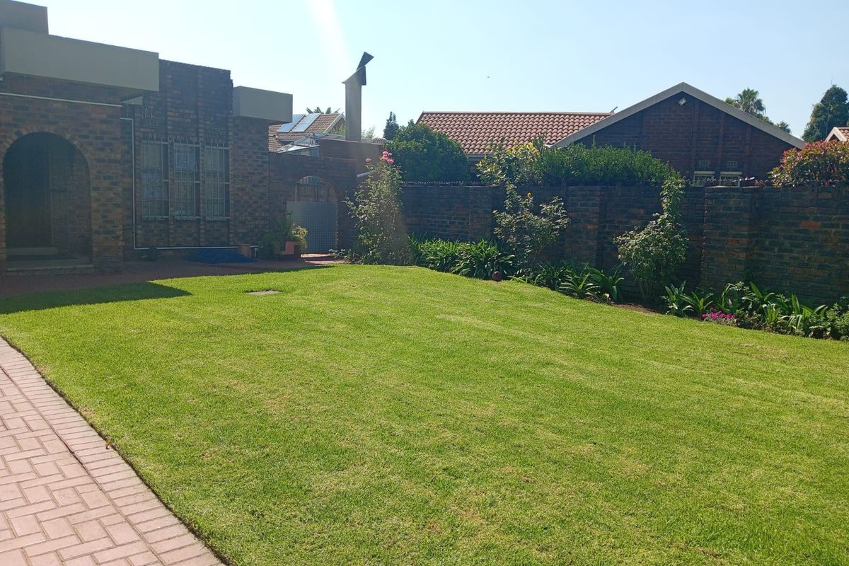 A well-maintained rear garden featuring a lush green lawn, brick boundary walls, and paved pathways adjacent to the house exterior.