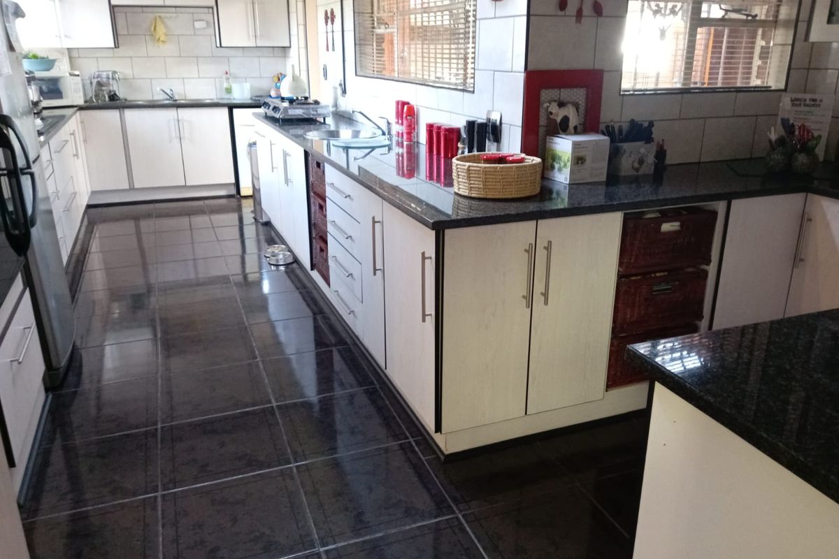 A functional kitchen featuring dark granite countertops, white cabinetry, tiled splashbacks, and dark floor tiles, providing ample workspace and storage.