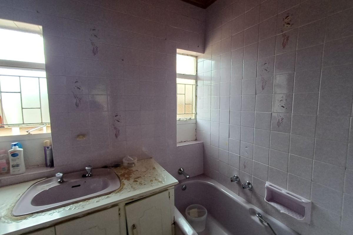 A dated bathroom featuring a built-in vanity with a basin and a bathtub, finished with light purple wall tiles and timber ceiling trim.