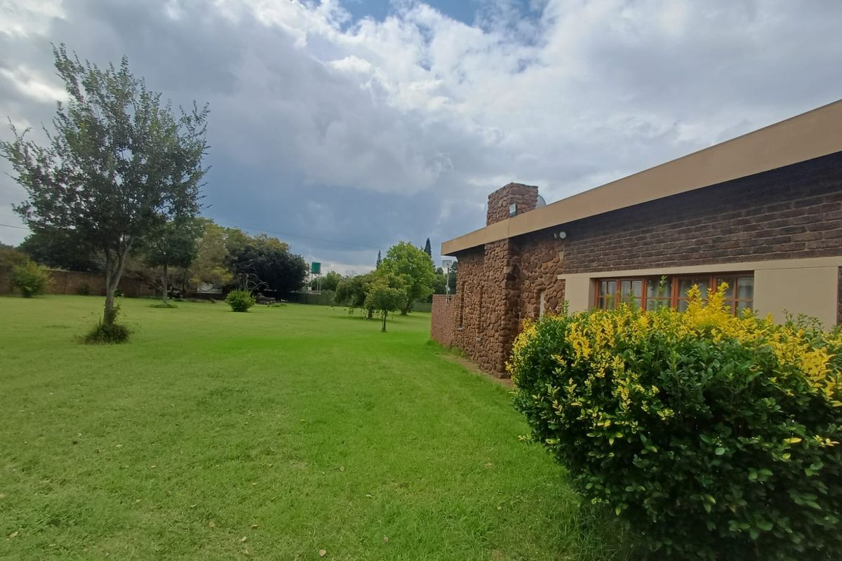 A view of the rear garden and the side elevation of the house, featuring stone masonry detailing and a large lawn area.