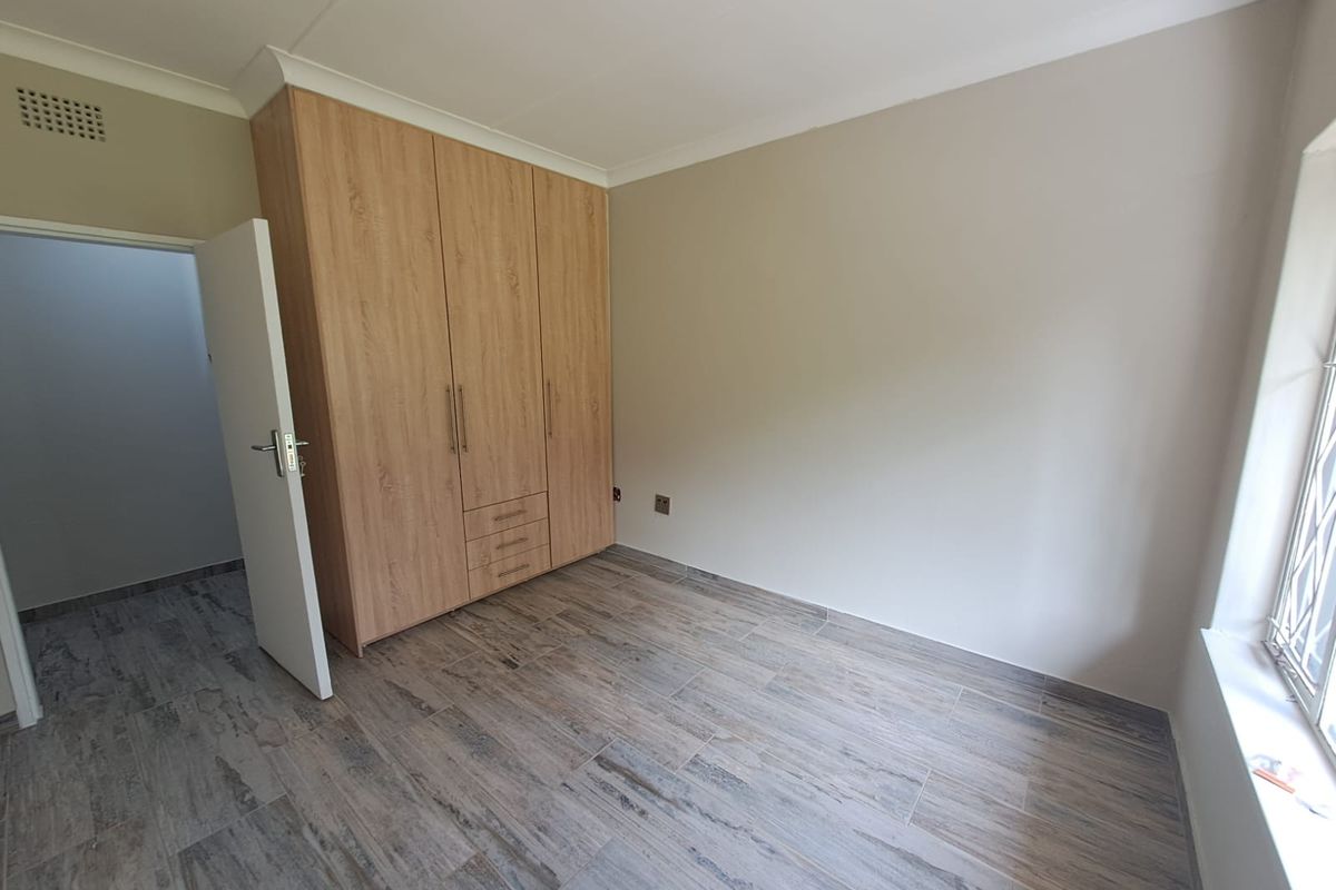 A bright bedroom featuring modern wood-look floor tiles and built-in wooden cabinetry with integrated drawers.