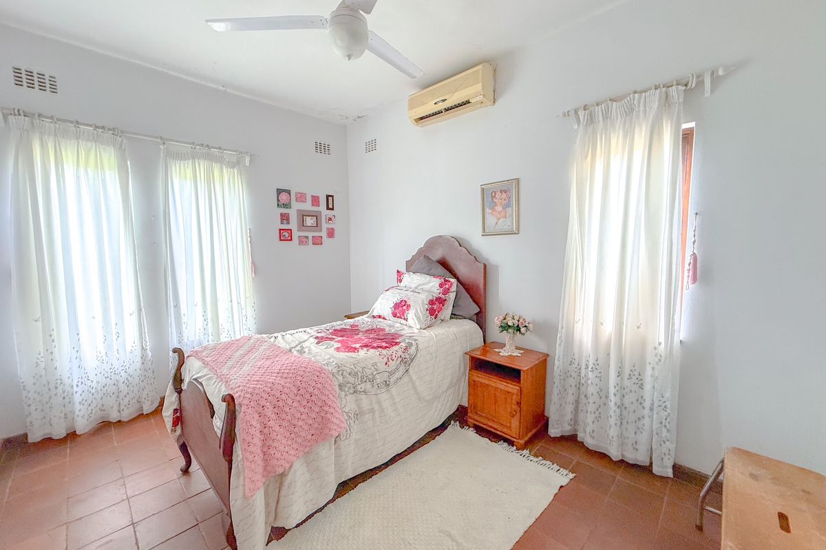 A bedroom featuring terracotta floor tiles, a ceiling fan, and a wall-mounted air conditioning unit, providing a functional and comfortable living space.