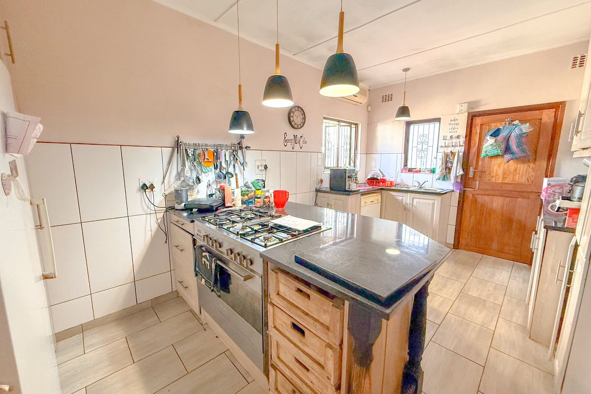 Functional kitchen featuring a central island with built-in gas hob and oven, tiled splashbacks, and ample cabinetry for storage.
