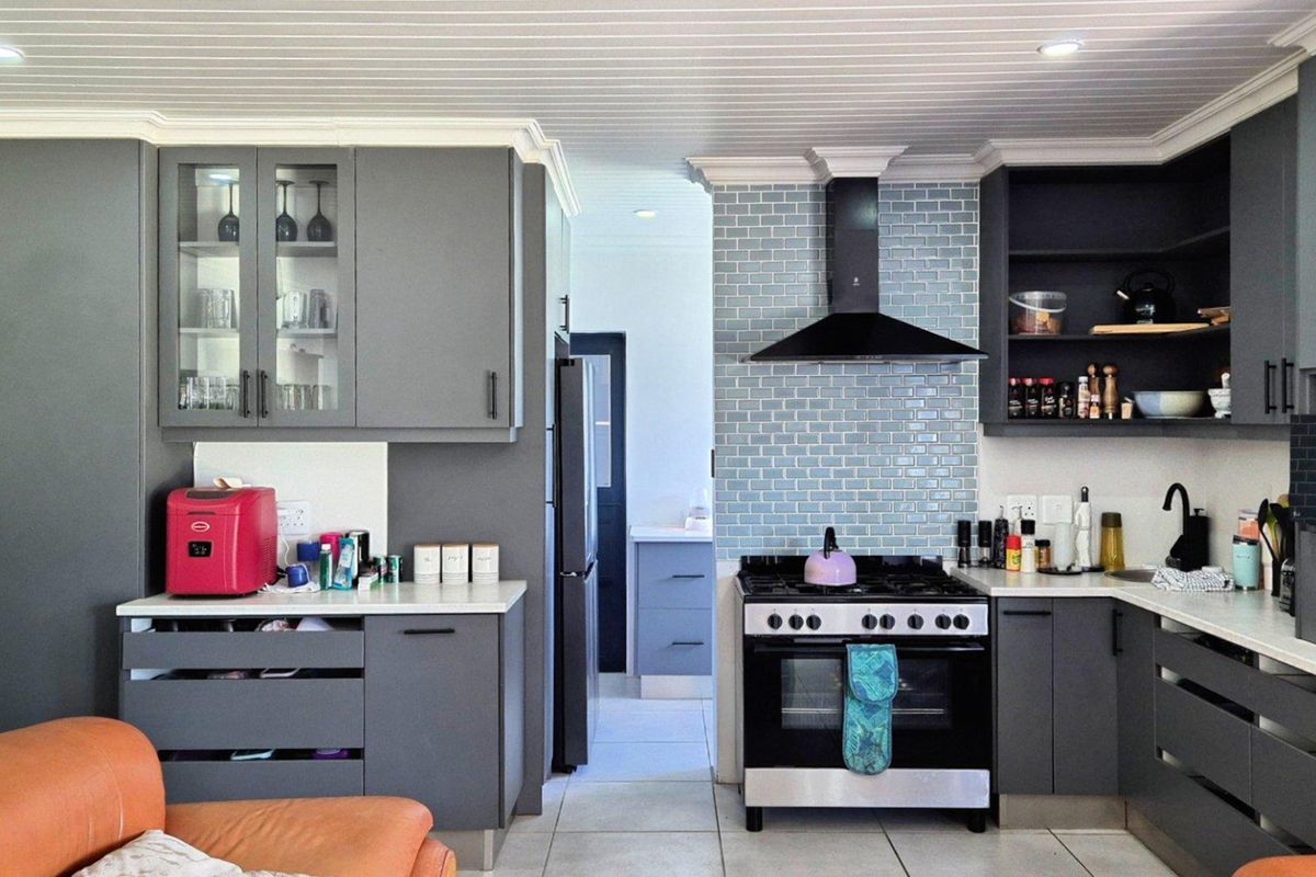 Modern kitchen featuring dark grey cabinetry, light blue subway tile backsplash, stainless steel gas stove, and a matching extractor fan.