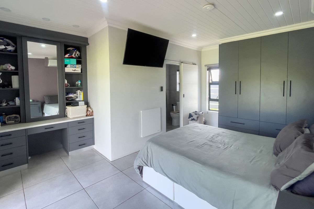 A modern bedroom featuring built-in grey cabinetry, a vanity area, tiled flooring, and an en-suite bathroom with a sliding door.
