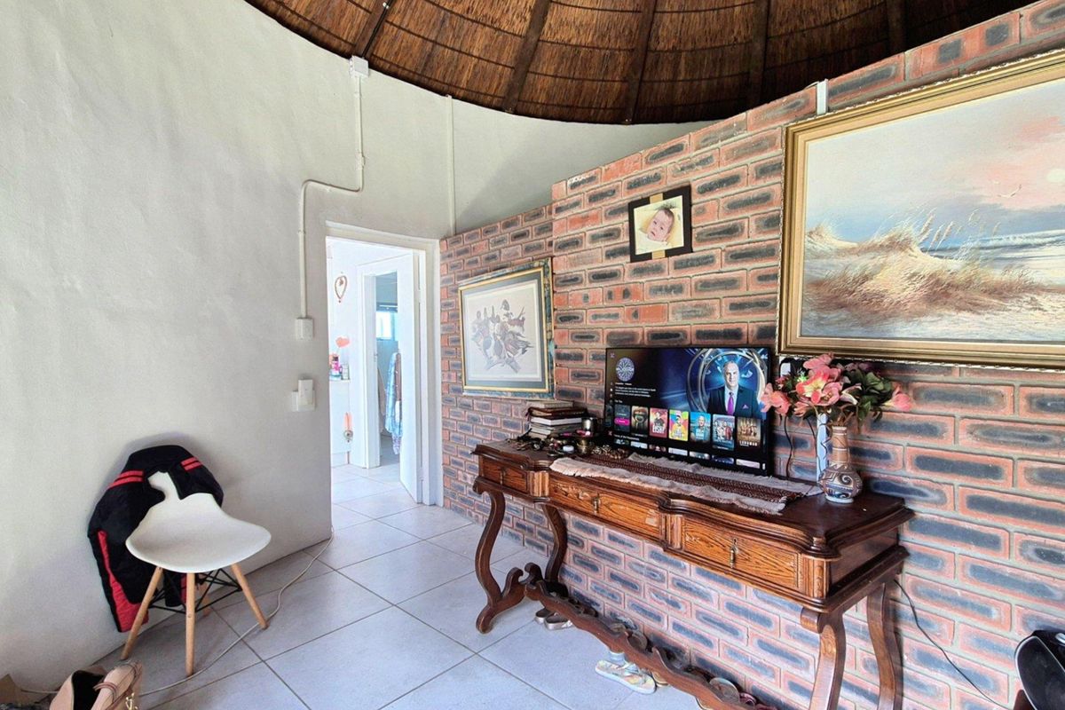 A living area featuring a distinctive thatched roof, exposed brick feature wall, and tiled flooring, providing a rustic and character-filled interior space.