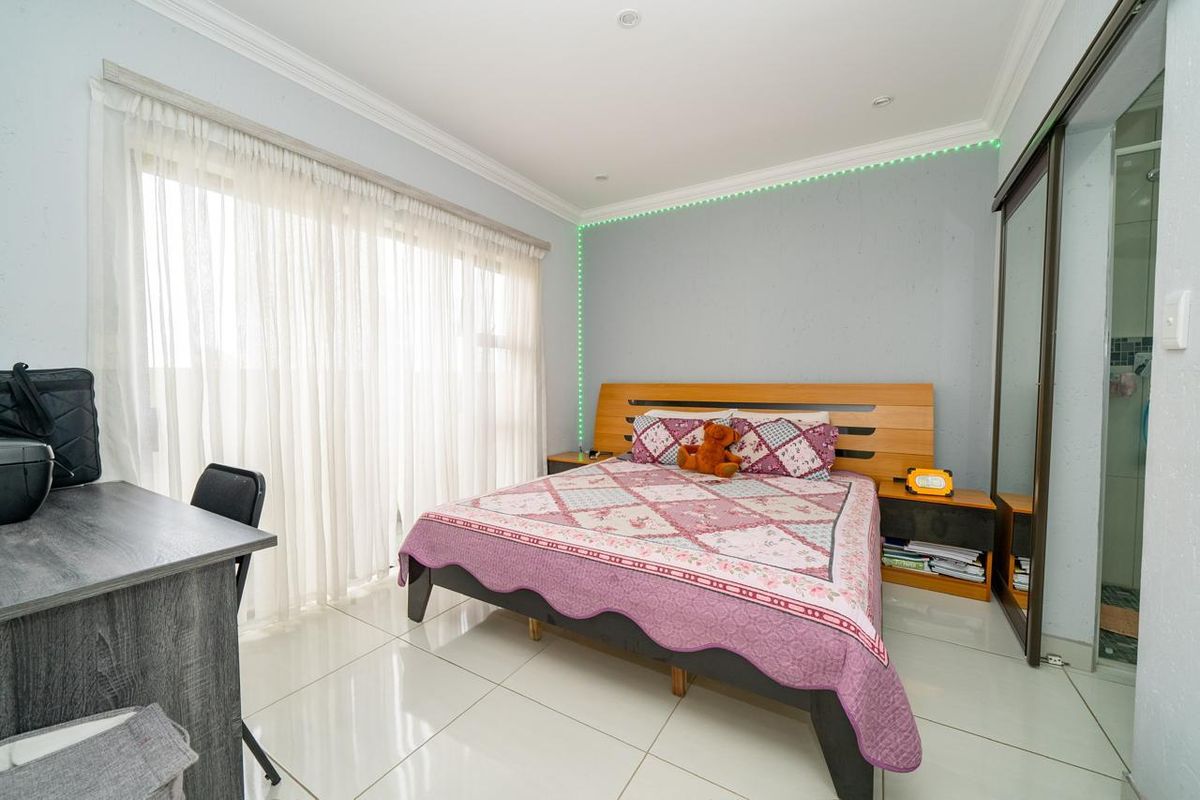 A well-maintained bedroom featuring tiled flooring, built-in sliding door cupboards, and large windows with sheer curtains, providing ample natural light.