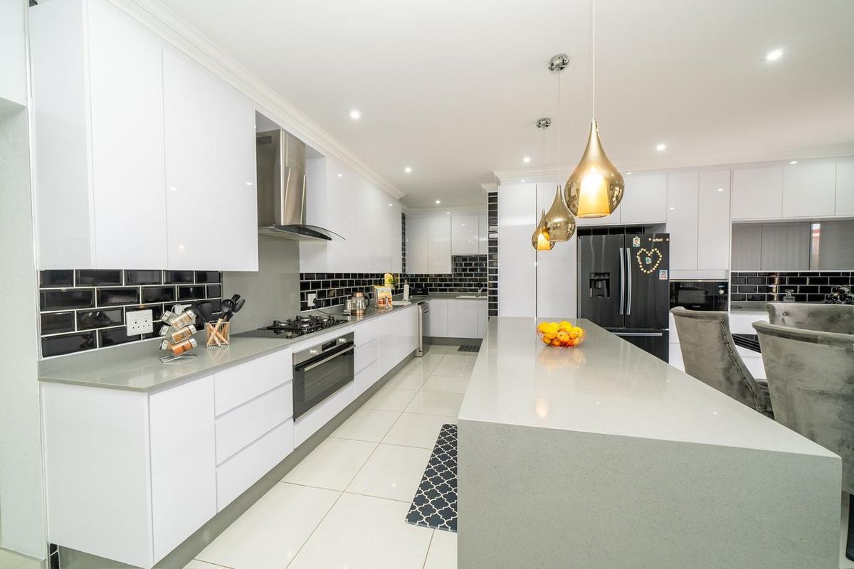 Modern kitchen featuring sleek white cabinetry, stone countertops, a large central island, built-in oven, gas hob, and stylish black subway tile backsplash.