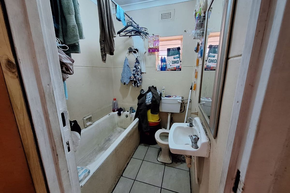 A compact bathroom featuring a standard bathtub, wall-mounted basin, and toilet, requiring significant cosmetic updates and maintenance to restore its functionality and appeal.
