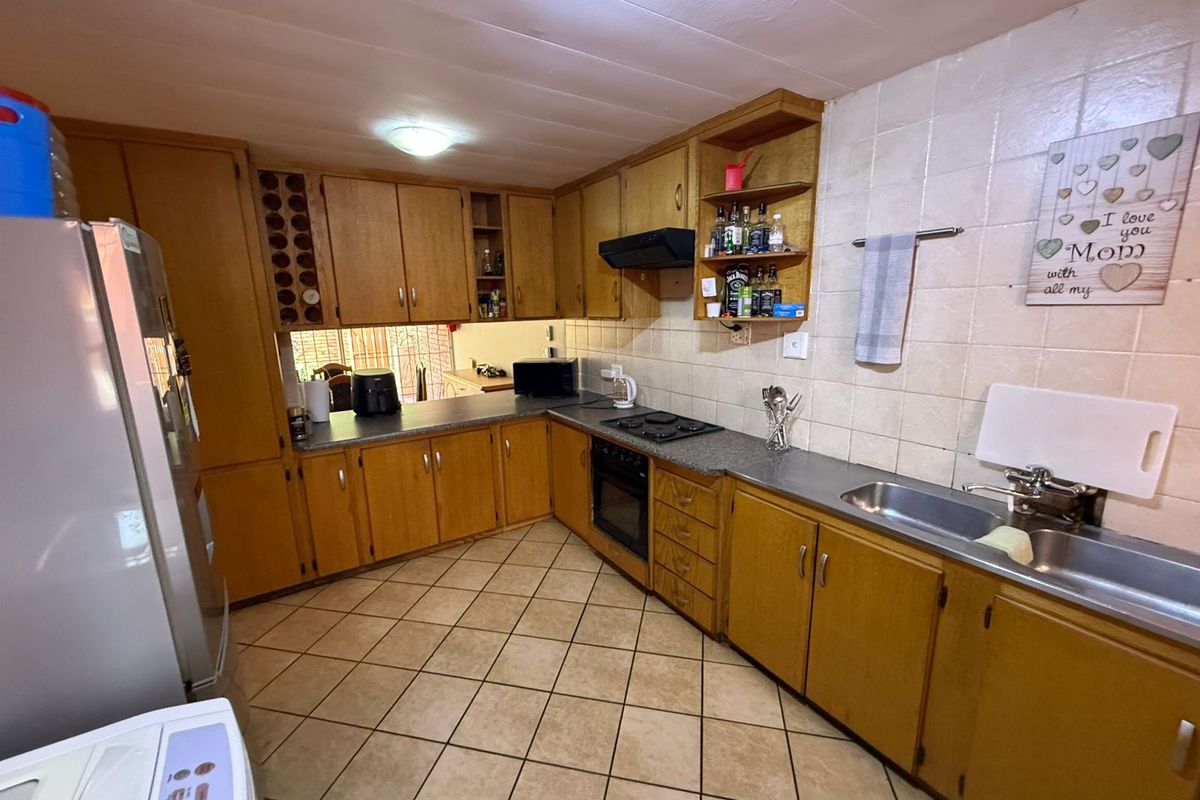 A functional kitchen featuring wooden cabinetry, built-in oven, hob, extractor fan, and a double basin sink with tiled backsplash and flooring.