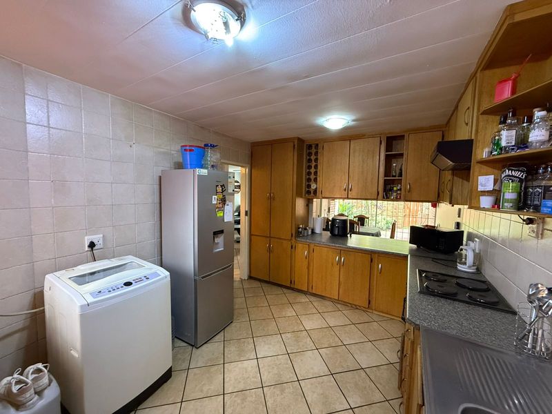 Functional kitchen featuring wooden cabinetry, laminate countertops, electric hob, extractor fan, and tiled flooring with a practical layout.
