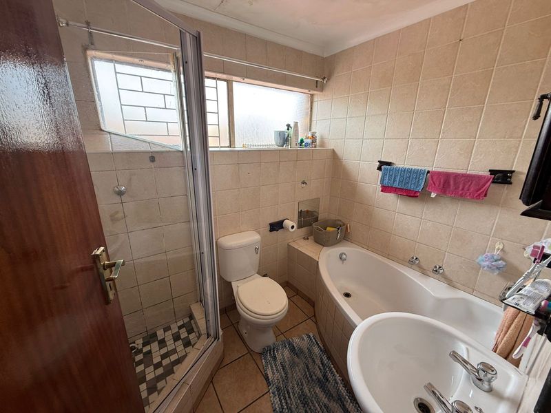 A dated bathroom featuring a shower enclosure, built-in bathtub, pedestal basin, and toilet with neutral wall and floor tiling.