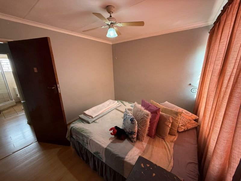 A cozy bedroom featuring laminate flooring, a ceiling fan, and neutral wall tones, with an adjacent view into a tiled bathroom area.