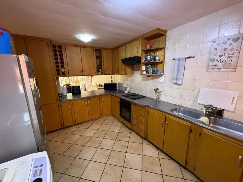 A functional kitchen featuring wooden cabinetry, built-in oven, hob, extractor fan, and a double basin sink with tiled backsplash and flooring.