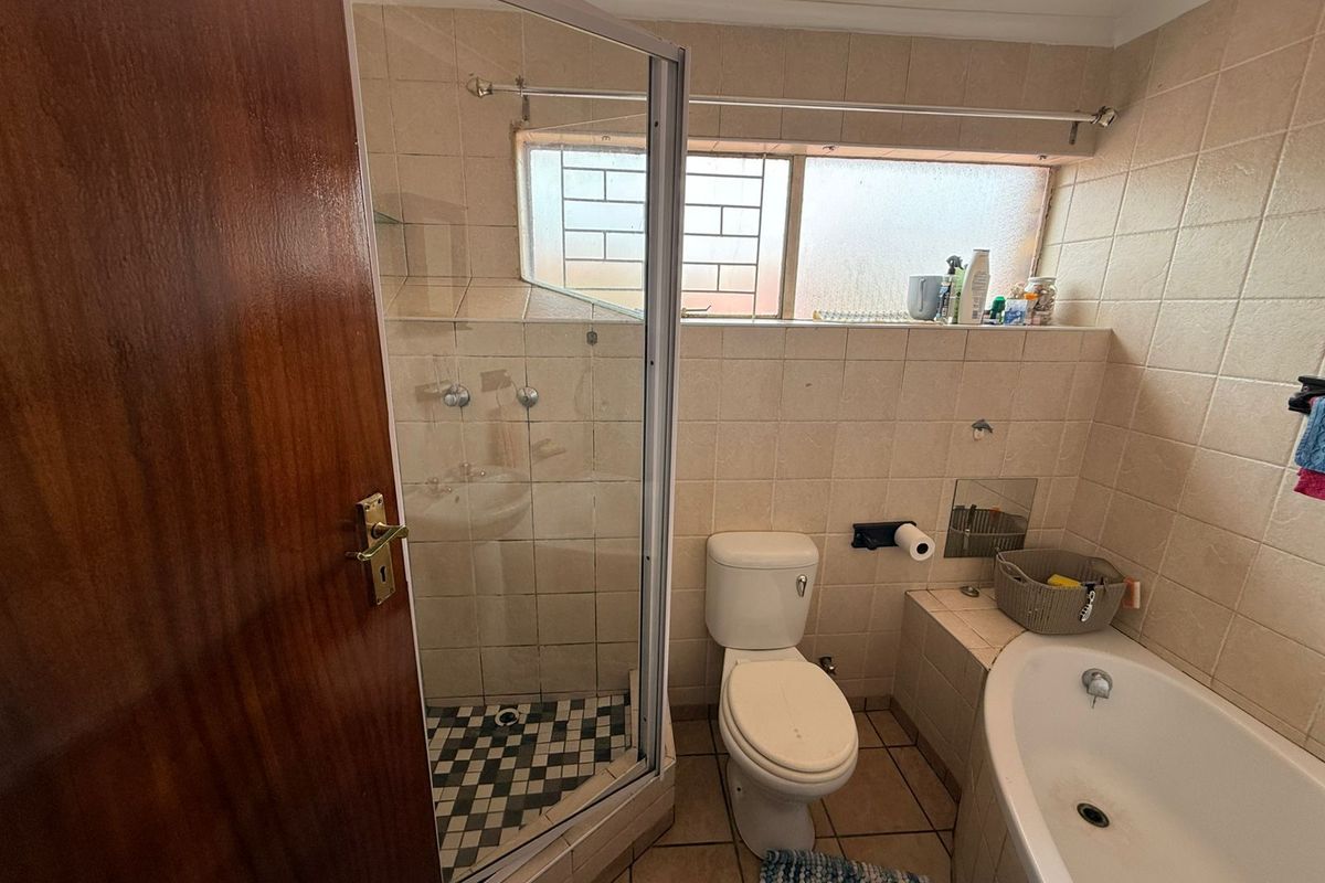 A dated bathroom featuring a corner shower enclosure, built-in bathtub, toilet, and tiled finishes, requiring cosmetic updates to modernize the space.