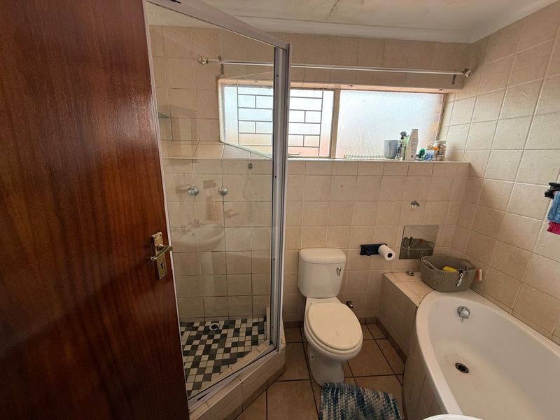 A dated bathroom featuring a corner shower enclosure, built-in bathtub, toilet, and tiled finishes, requiring cosmetic updates to modernize the space.