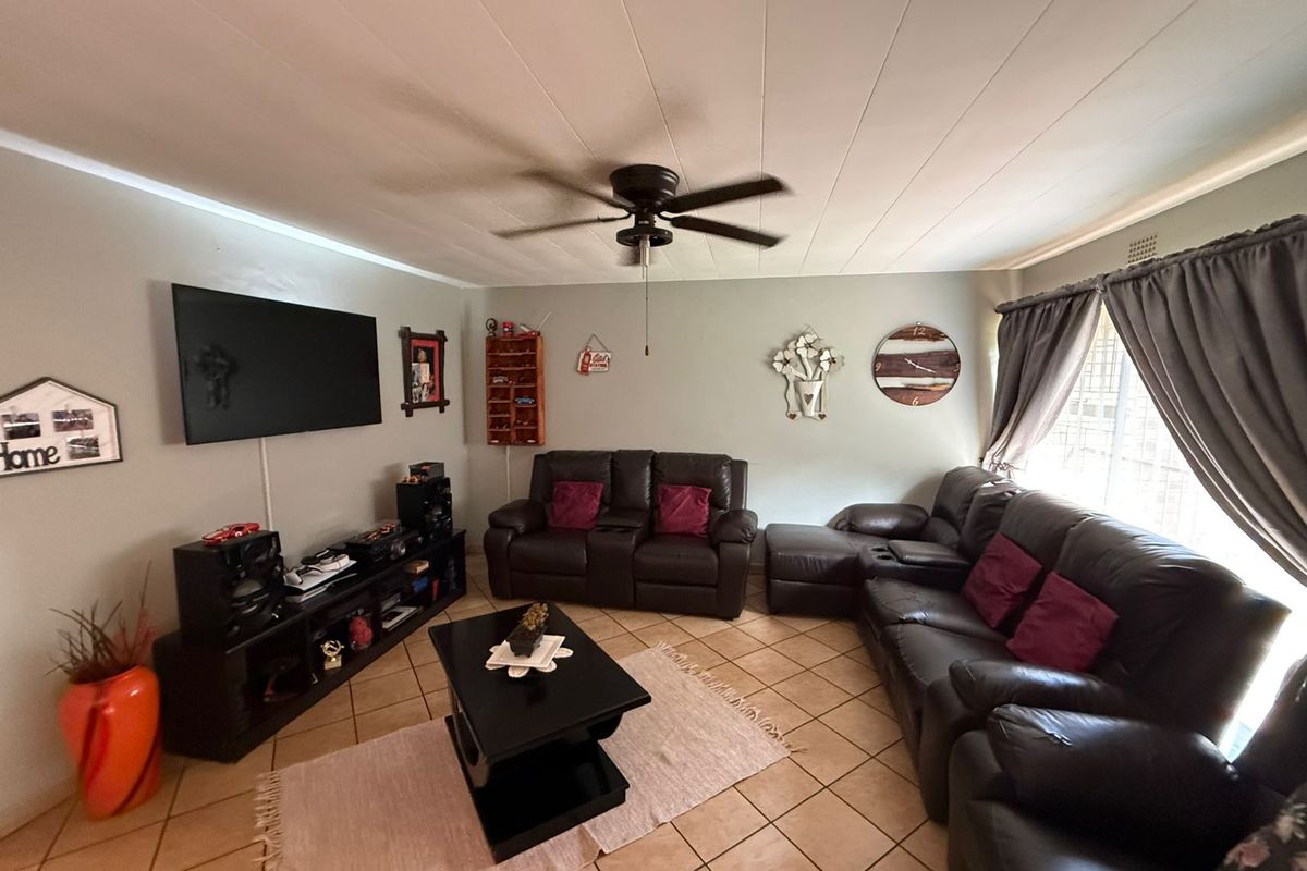 A comfortable living room featuring tiled flooring, a ceiling fan, and large windows with curtain rails, providing a functional and well-lit space.
