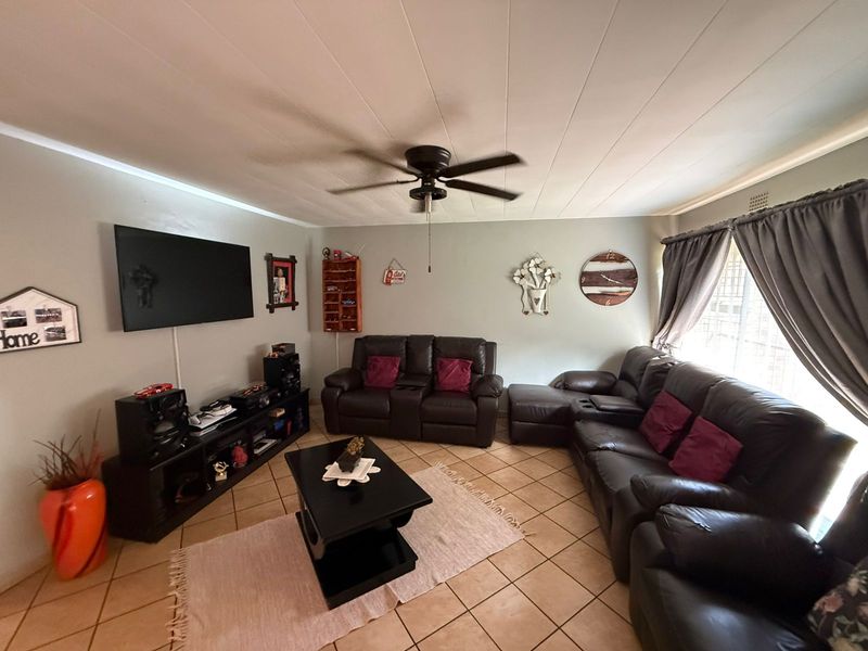 A comfortable living room featuring tiled flooring, a ceiling fan, and large windows with curtain rails, providing a functional and well-lit space.
