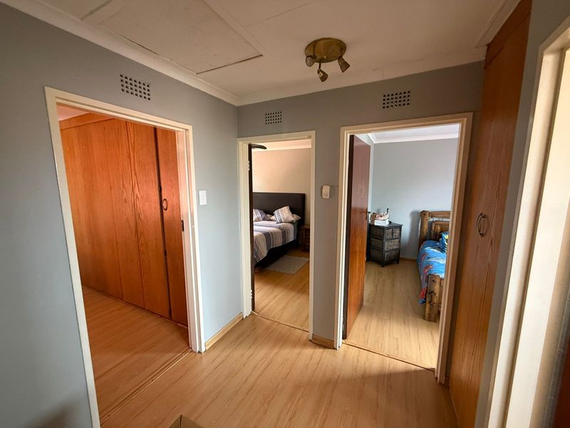 A functional hallway featuring laminate flooring and built-in wooden cupboards, providing access to multiple bedrooms.