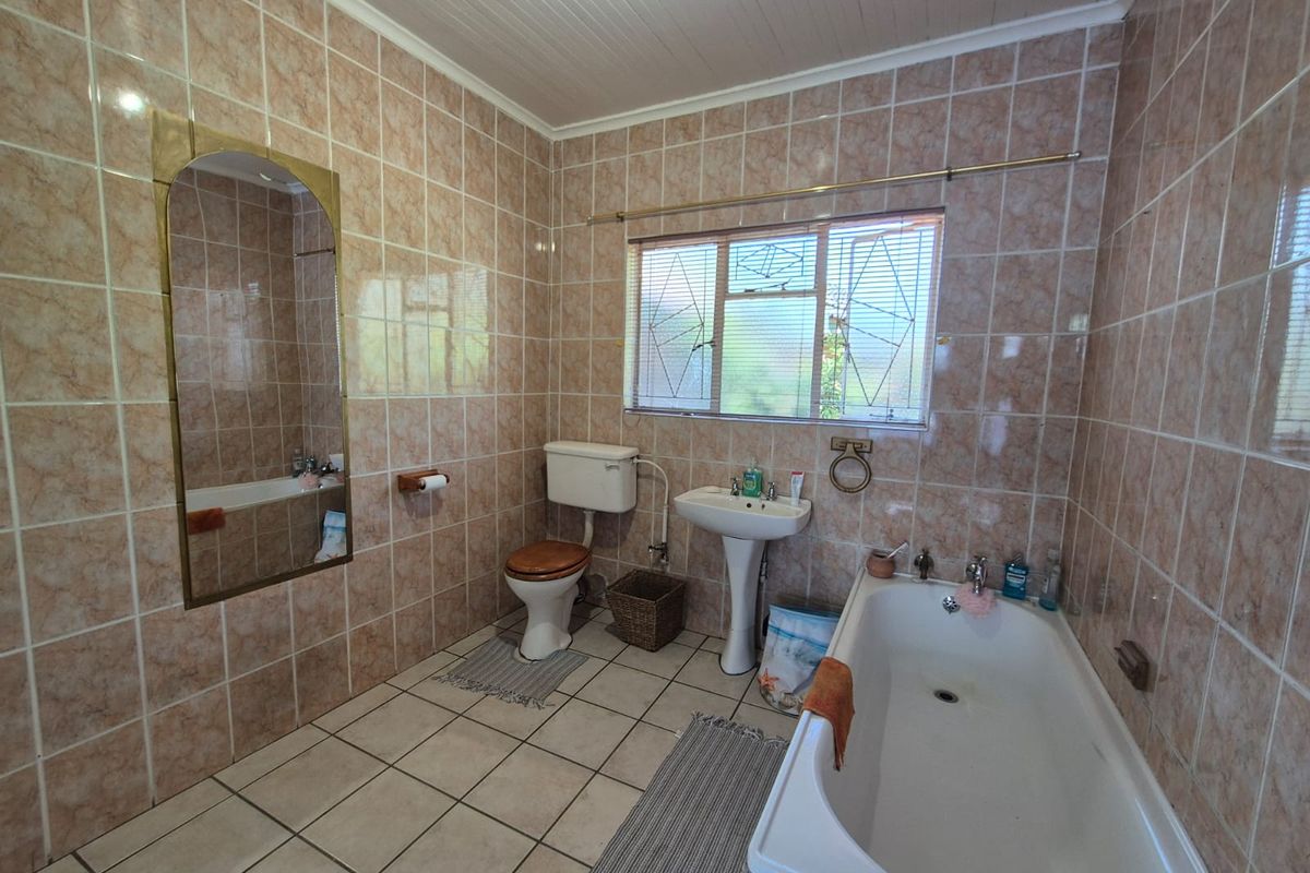 A functional bathroom featuring a bathtub, pedestal basin, and toilet, finished with full-height wall tiling and tiled flooring.