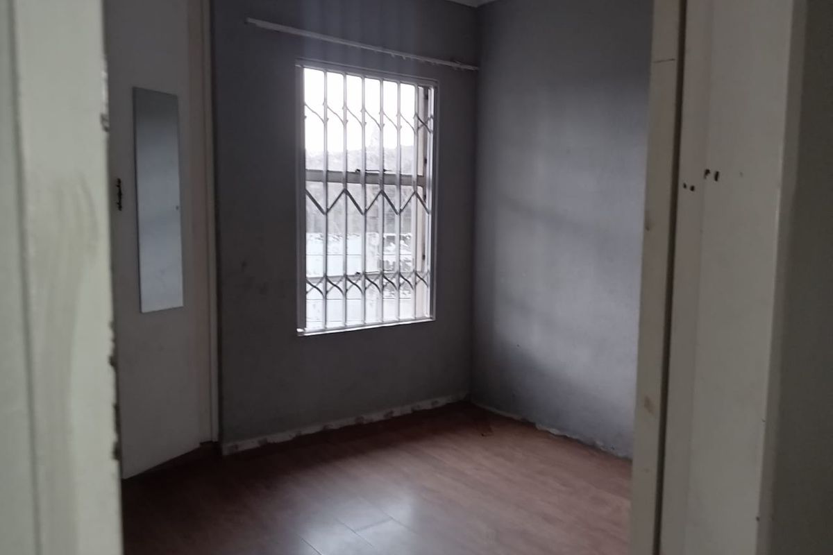 An empty bedroom featuring laminate flooring, grey walls, and a window fitted with security bars.