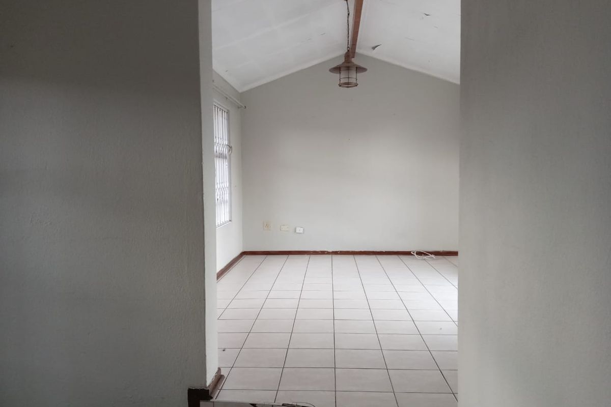 An empty living room featuring tiled flooring, a vaulted ceiling with a pendant light, and security bars on the window.