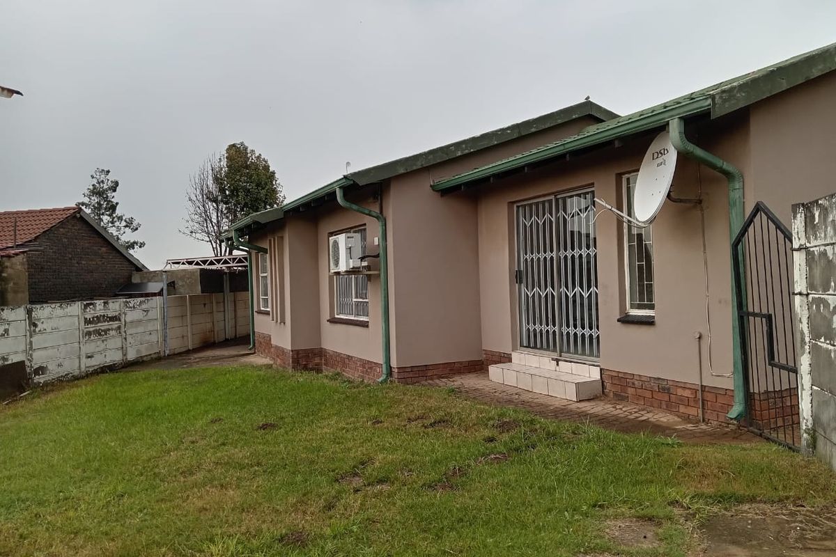 Rear view of the property featuring a brick and plaster facade, security gate, and a private garden area with boundary walling.