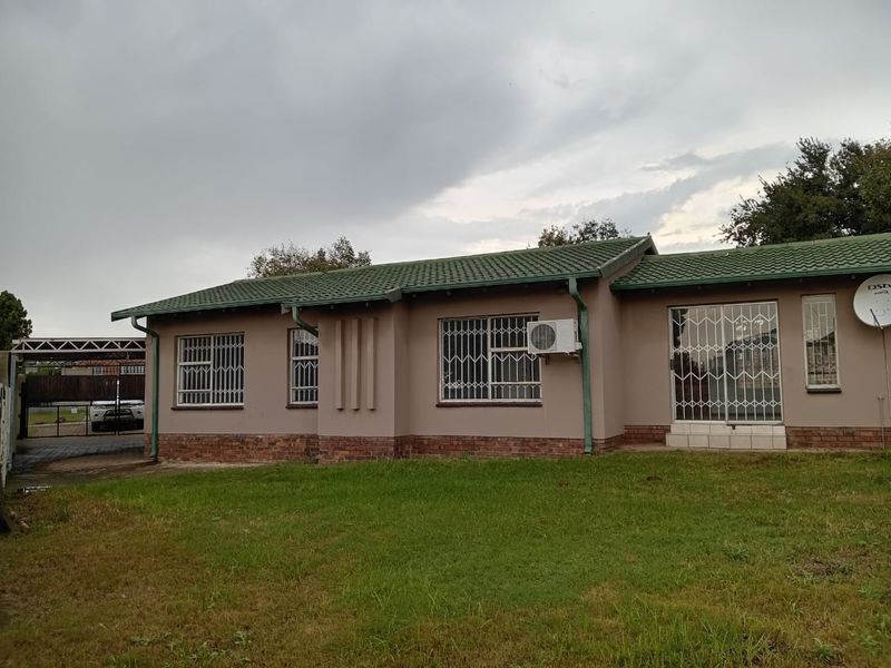 Front view of a single-story house featuring a tiled roof, brick base, security bars on windows, and an attached carport.